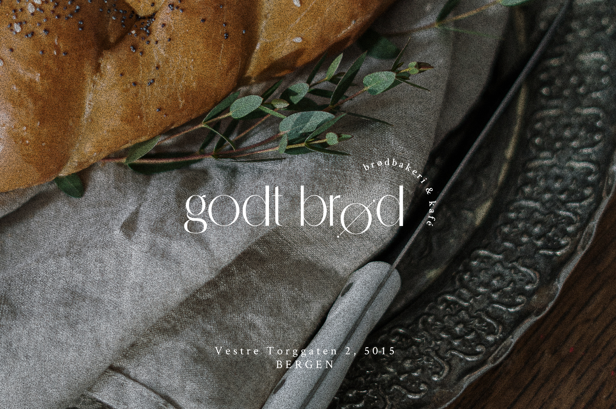 Close up of a piece of poppy bread on a light grey cloth, an angled bread knife and vintage silver platter. A white Godt Brod logo is centered on top of the image.