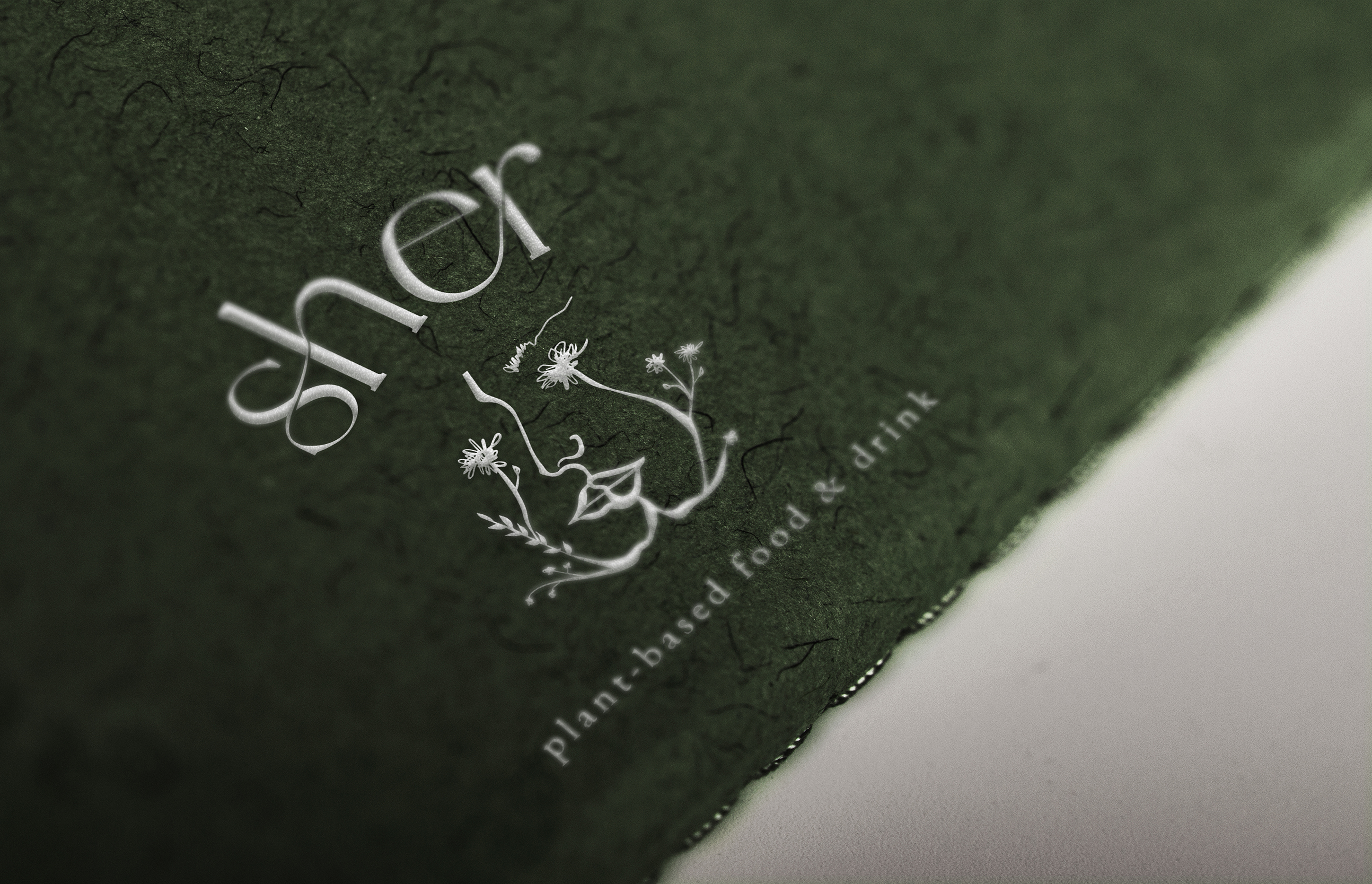 Close up shot of the Sher logo on dark green paper